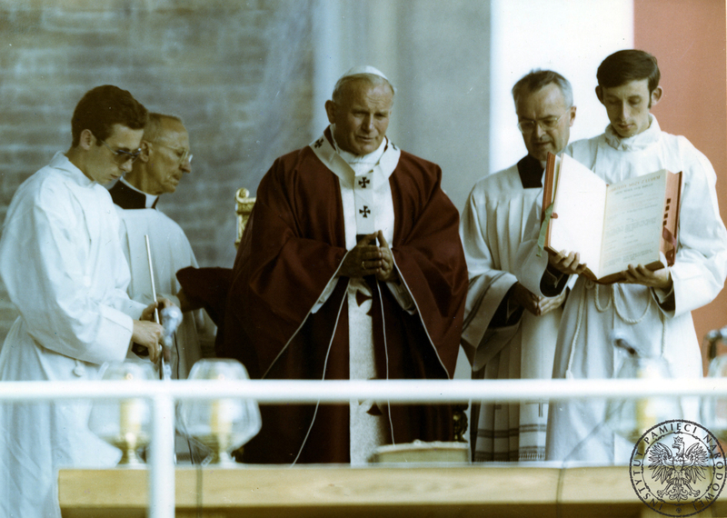 Jan Paweł II za ołtarzem polowym na Wzgórzu Lecha w  czasie koncelebry mszy świętej. Pierwszy z lewej ceremoniarz papieski Orazio Cocchetti, drugi z prawej ceremoniarz papieski ksiądz Virgilio Noe. 3 VI 1979 r. Sygnatura: IPNPO-7-7-1-14