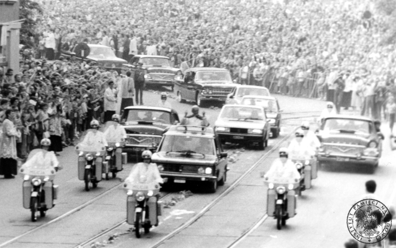 Przejazd kolumny papieskiej ulicą Krakowską prawdopodobnie w drodze z Wawelu na Skałkę. Jan Paweł II pozdrawia wiernych z samochodu specjalnego Fiat 130 otoczonego przez asystę motocyklistów Milicji Obywatelskiej. 8 VI 1979 r. Sygnatura: IPNKr-7-7-5-7