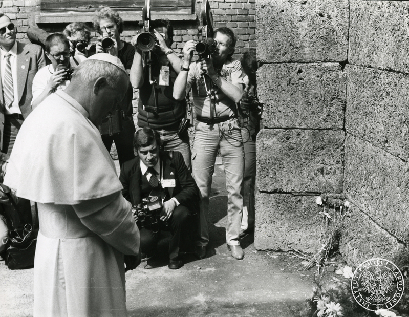 Jan Paweł II modli się przed ścianą straceń na terenie byłego niemieckiego nazistowskiego obozu koncentracyjnego i zagłady Auschwitz-Birkenau w Oświęcimiu. Za papieżem fotoreporterzy i operatorzy kamer, wśród nich Arturo Mari (kuca), Sygnatura: IPNPo-7-7-1-41