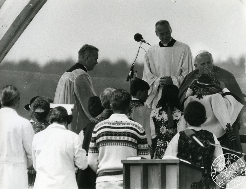 Dzieci w strojach góralskich składają dary na ręce Jana Pawła II w czasie mszy świętej  odprawianej na płycie lotniska, obok papieża jego ceremoniarz  ksiądz Orazio Cocchetti. Sygnatura: IPNPo-7-7-1-70